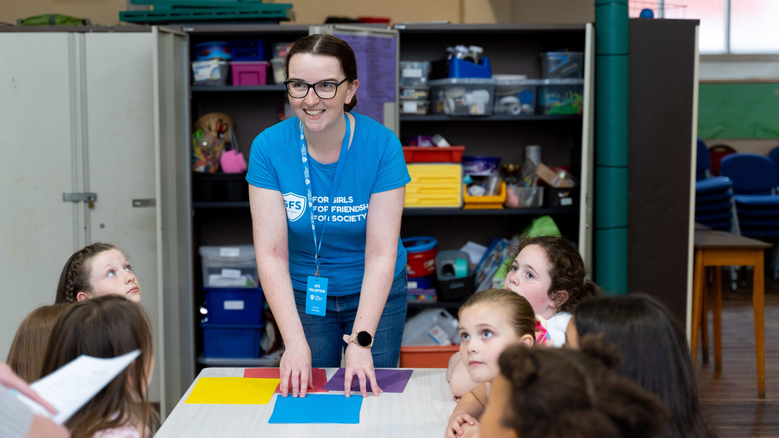 volunteer leading a session, standing at table surrounded by girls